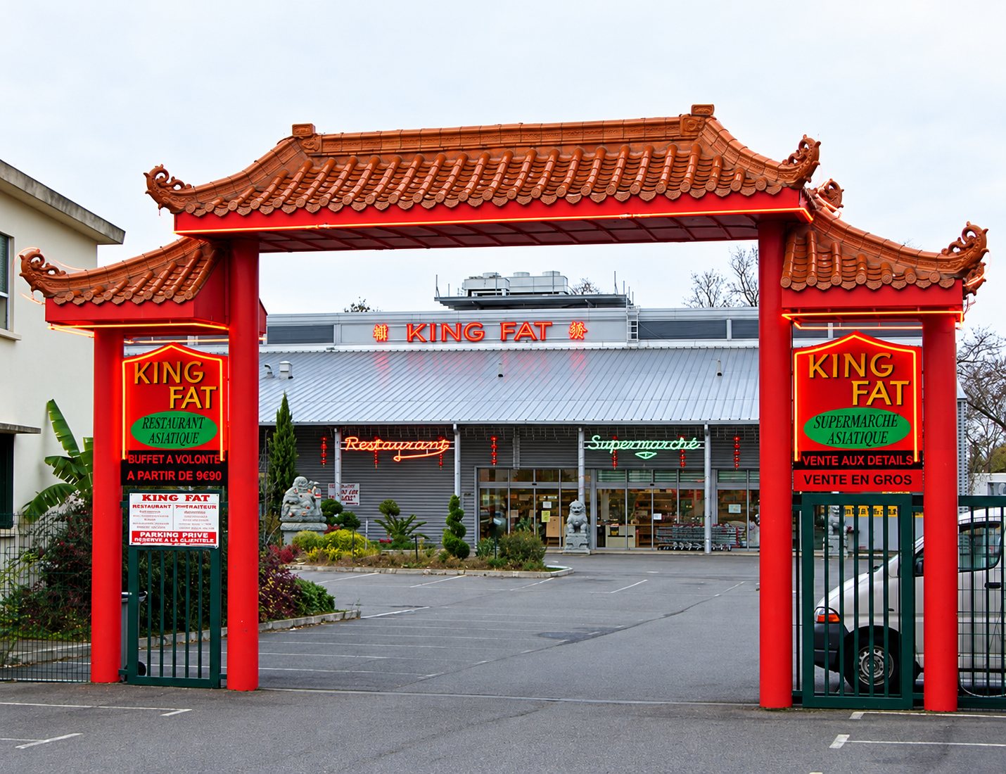 Entrée du supermarché King Fat à Montaudran : portique rouge à toit de tuiles et parking